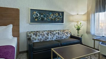 A hotel room with a bed, a sofa, a coffee table, a lamp, and a wall art piece.