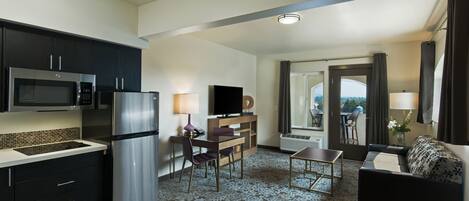 Una habitación de hotel moderna con kitchenette, zona de comedor, sofá y balcón con vistas.