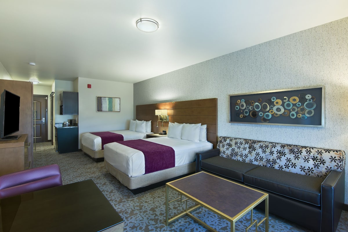 Ein Hotelzimmer mit zwei Betten, einem Schlafsofa, einem kleinen Tisch und einem Fernseher.
