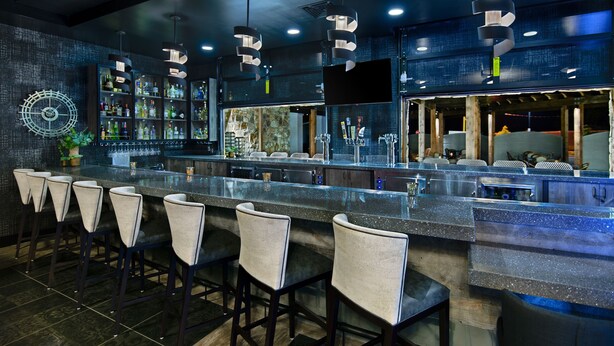 A bar area with a long counter, multiple stools, and a variety of bottles and glasses.