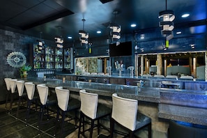 A bar area with a long counter, multiple stools, and a variety of bottles and glasses.