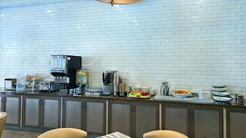 Una barra de desayuno con una cafetera, un bol de fruta y diversas opciones para el desayuno.