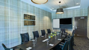 Une salle de conférence avec une longue table, des chaises, un écran de projection et une porte.