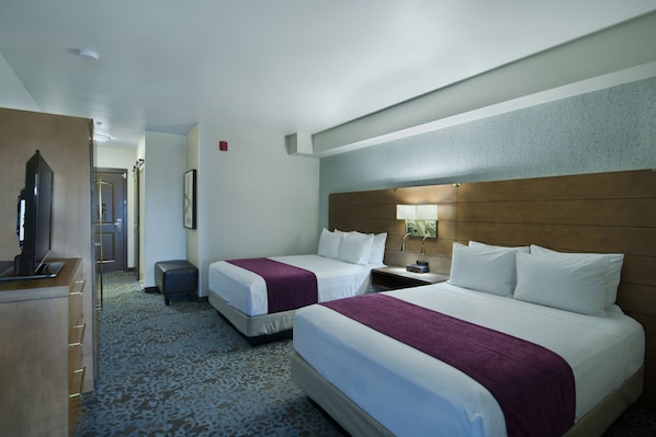 Une chambre d’hôtel avec deux lits, un bureau, une télévision et une salle de bain que l’on aperçoit à l’arrière-plan.