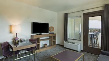 Ett hotellrum med en platt-TV, ett matbord med stolar, ett litet bord, en soffa, ett fönster med utsikt och en luftkonditioneringsanläggning.