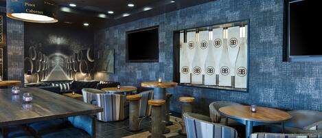 A modern restaurant interior with high tables, cushioned booths, and a patterned wall.