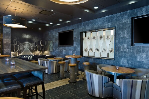 A modern restaurant interior with high tables, cushioned booths, and a patterned wall.