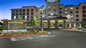 A hotel entrance with a sign for Oxford Suites, a large building with multiple floors, and a landscaped area with plants and a curb.