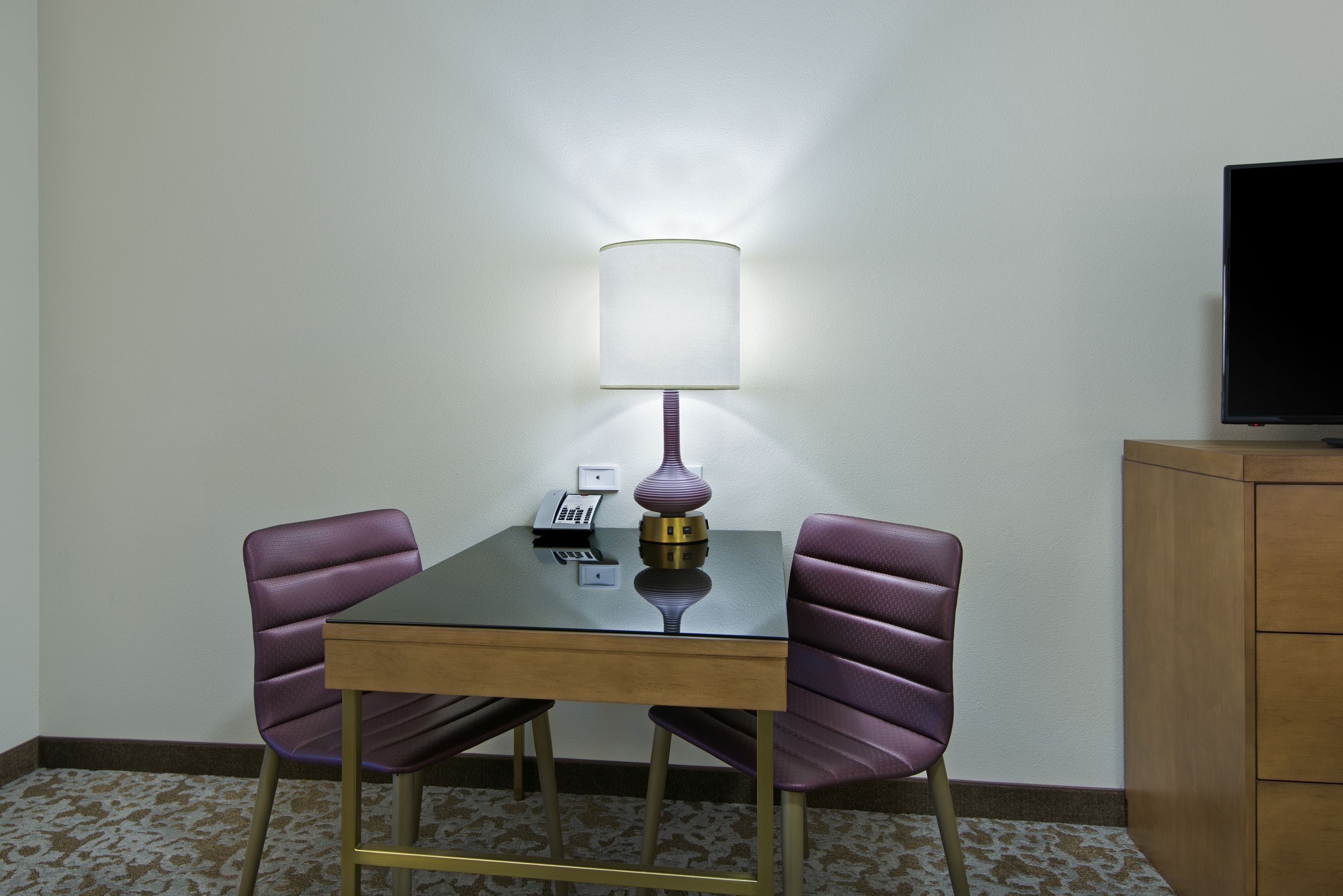 Ein kleines Zimmer mit einem Tisch, zwei Stühlen, einer Lampe, einem Telefon und einem Fernseher.