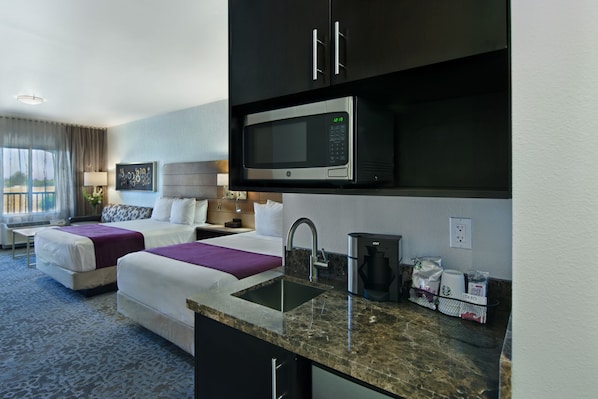 A hotel room with two beds, a kitchenette, a sink, and a large window.