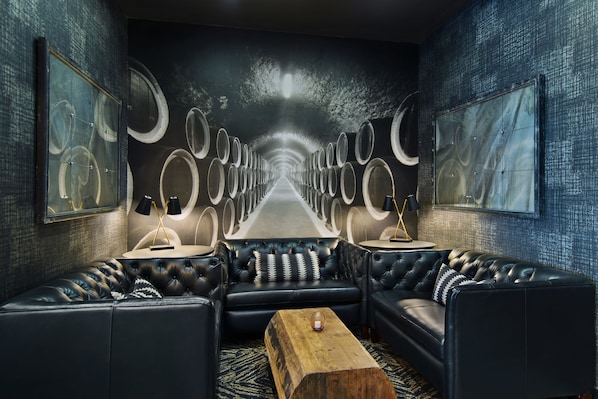 A modern lounge with leather sofas, a wooden coffee table, and a mural of barrels on the wall.