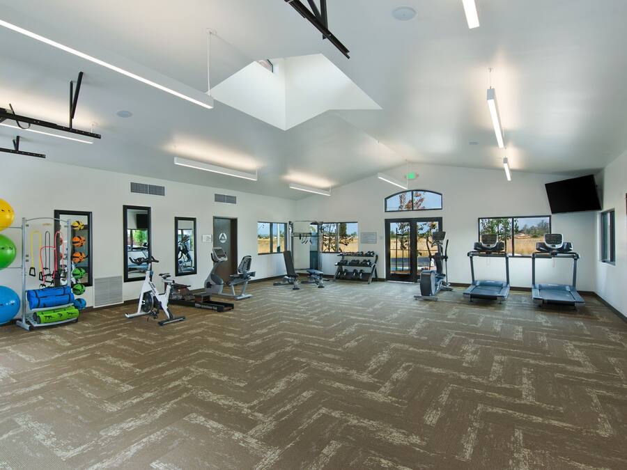 A spacious gym with exercise equipment, large windows, and a high ceiling.