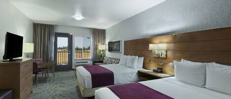 A hotel room with two beds, a desk, a TV, and a balcony with curtains.