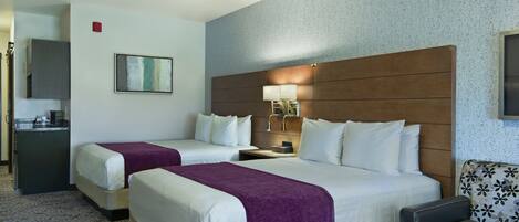 A hotel room with two beds, a desk, a chair, and a small table.