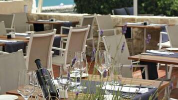 Ein Restaurant mit Terrassensitzgelegenheiten, Tische gedeckt mit Weingläsern und einer Flasche, und Blick aufs Meer.