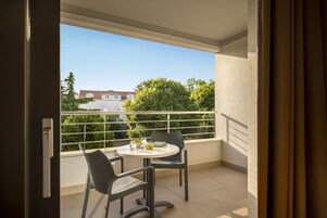 Un balcón con mesa y sillas, vistas a zonas verdes y edificios, y un techo de malla.