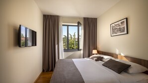 A hotel room with a bed, a TV mounted on the wall, a window with curtains, and a framed picture on the wall.