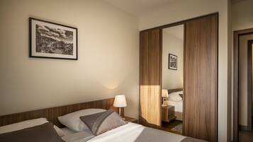 Quarto de hotel com cama, mesa de cabeceira, abajur, quadro pendurado na parede e guarda-roupa de madeira.