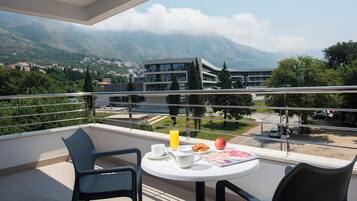 Un balcón con una mesa dispuesta para el desayuno, con vistas a un paisaje montañoso y un edificio moderno.