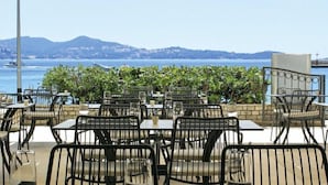 An outdoor dining area with tables and chairs, overlooking a body of water and hills.