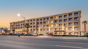 A multi-story hotel with a uniform exterior, balconies, and a parking lot with several cars. - Best Western Plus Galveston Suites (Galveston)