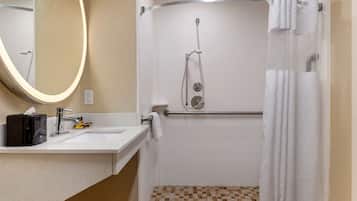A bathroom with a white sink, a mirror with a light, a shower with a glass door, and a tiled floor.