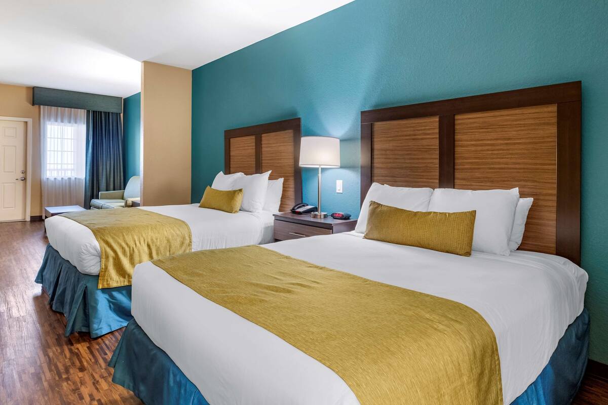 A hotel room with two beds, a nightstand, a lamp, and a window with curtains.