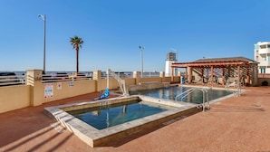 A pool area with two pools, a covered seating area, and a view of the ocean. - Best Western Plus Galveston Suites (Galveston)