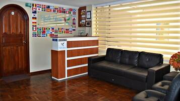 A reception area with a wooden door, a reception desk, and a black leather sofa. Flags are displayed on the wall above the desk.