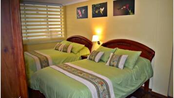 Una habitación de hotel con dos camas, cada una con ropa de cama verde y almohadas decorativas. Hay una lámpara de pared en el lado derecho de la cama.
