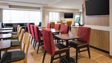 A hotel lobby with multiple tables and chairs, a reception desk, and a large TV screen.