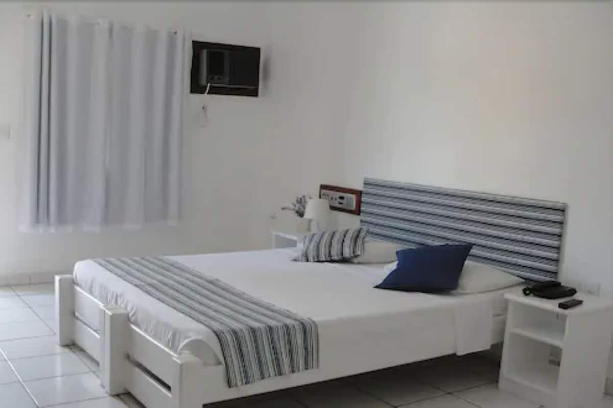 Ein modernes Schlafzimmer mit Bett, Nachttischen, Fernseher und einem Fenster mit Vorhängen.