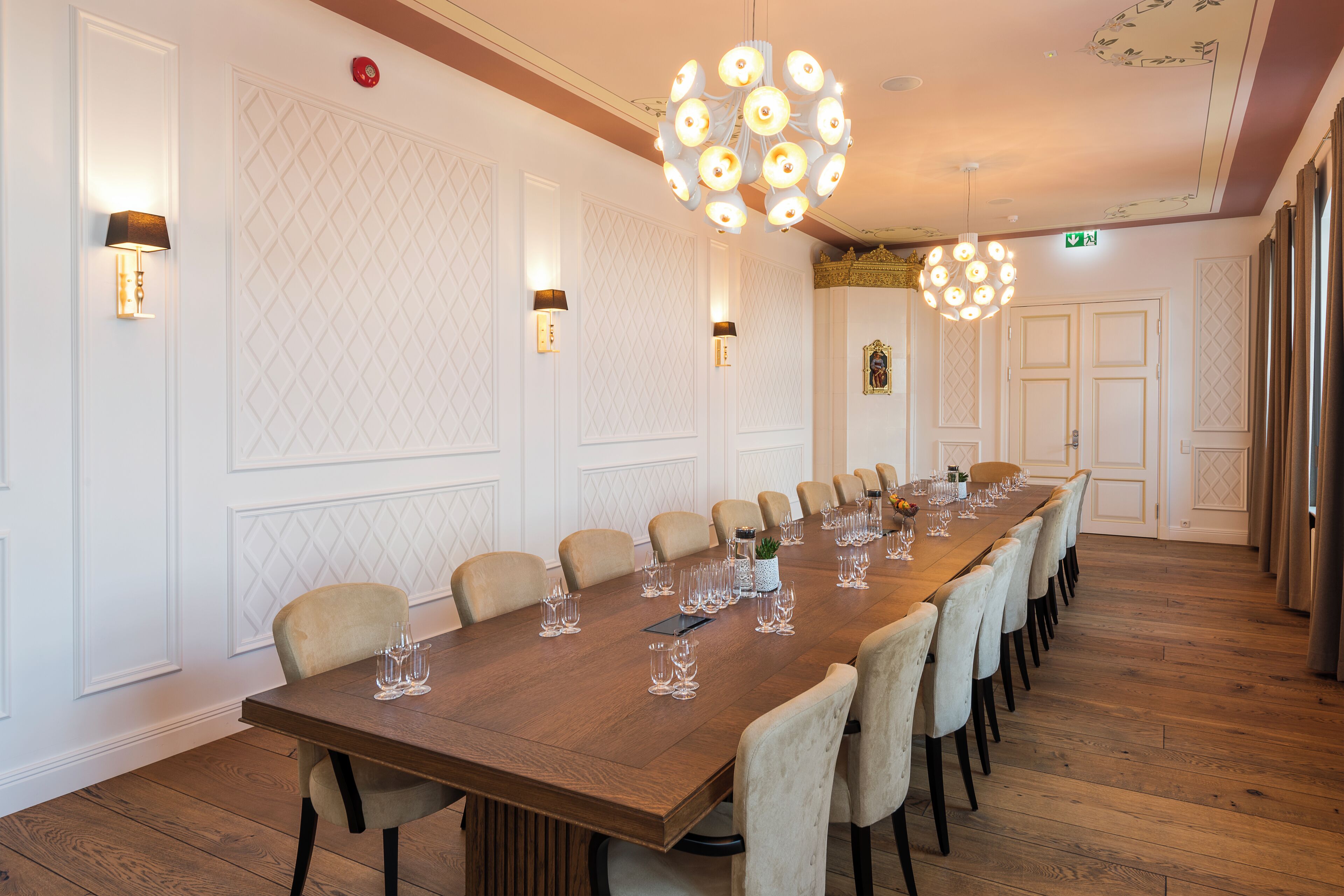 Un salón de conferencias con una larga mesa de madera, sillas color beige y luminarias fijadas a la pared.
