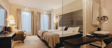 A hotel room with a bed, bedside table, lamp, chair, and a large mirror.