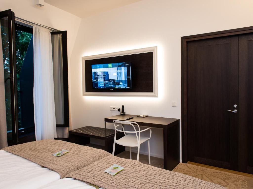 Une chambre d’hôtel comprenant un lit, un bureau, une chaise, un téléviseur fixé au mur et une porte.