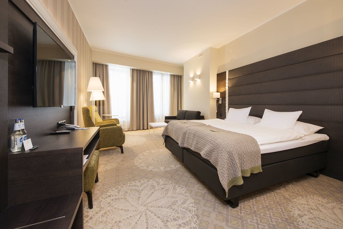 Ein Hotelzimmer mit einem großen Bett, einem Schreibtisch, einem Stuhl und einem Fernseher.