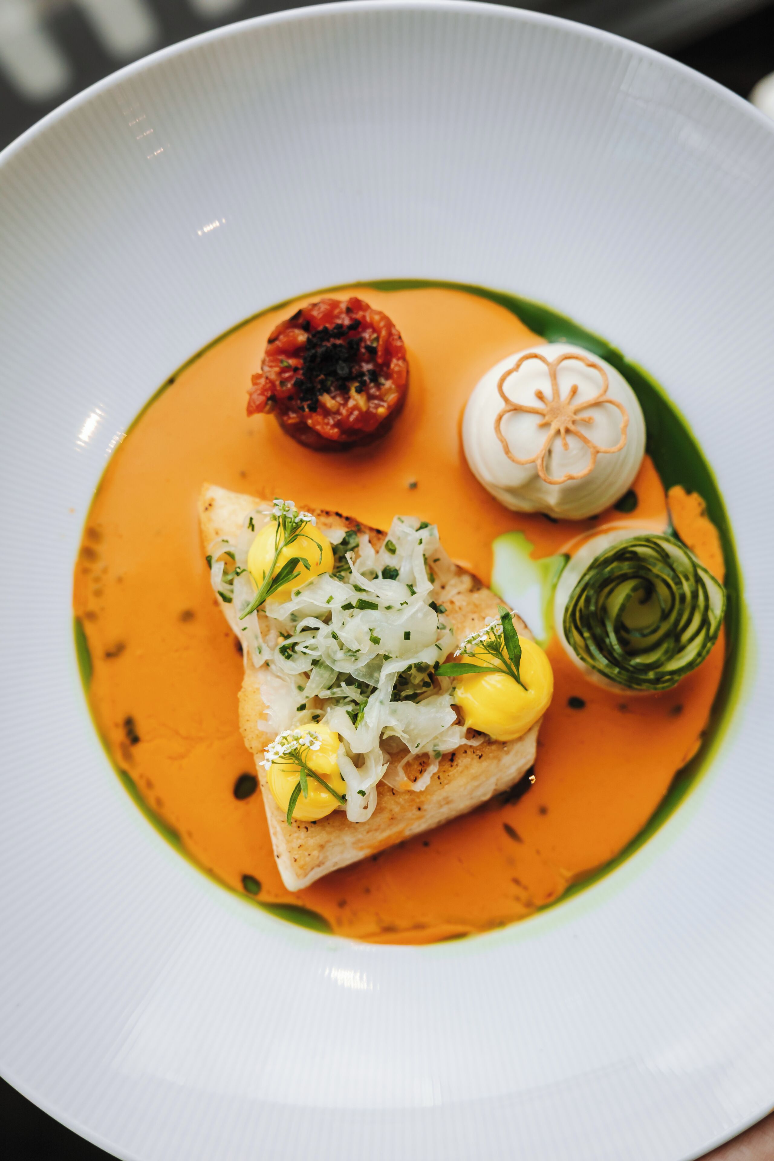 A plate with a fish fillet, a dollop of sauce, and a small vegetable garnish.
