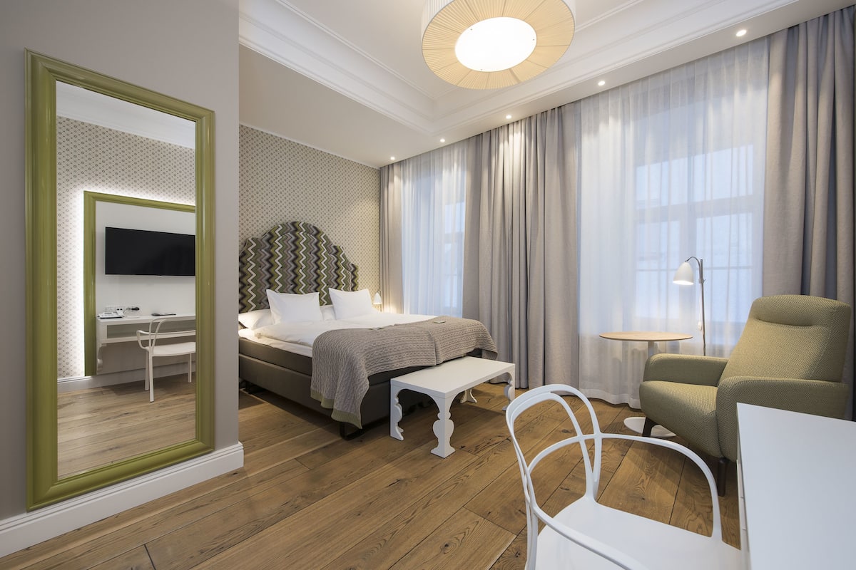 Ein modernes Hotelzimmer mit Bett, Nachttisch, Stuhl und einem großen Spiegel.
