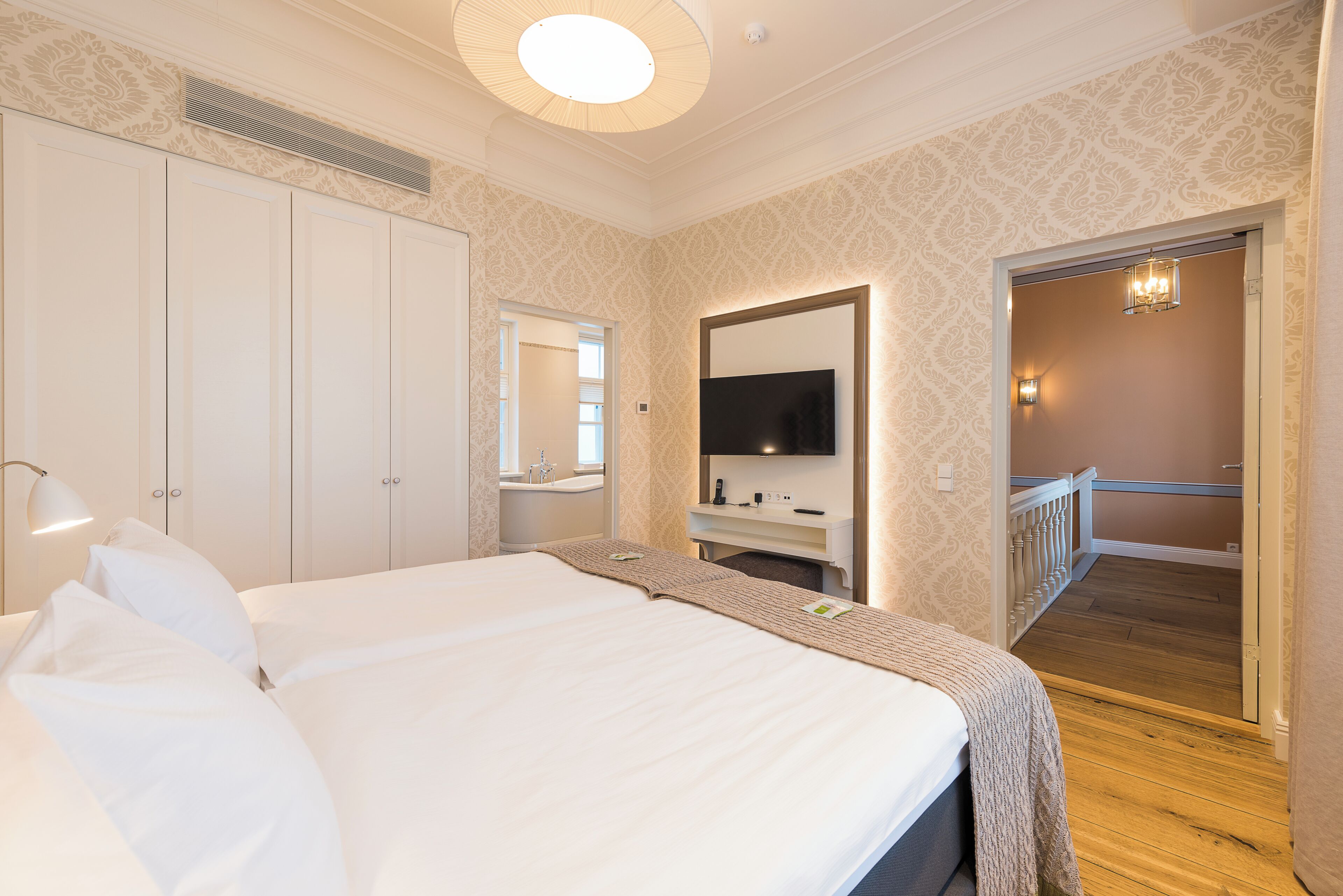 A hotel room with a large bed, a flat-screen TV, a bathroom with a bathtub, and a staircase leading to an upper floor.