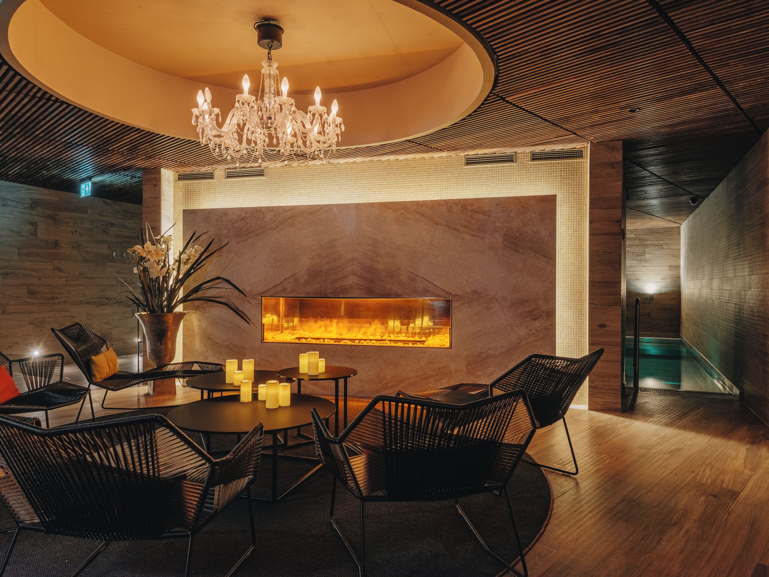 A modern interior with a round dining table, black chairs, a chandelier, and a wall-mounted fireplace.