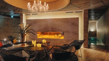 A modern interior with a round dining table, black chairs, a chandelier, and a wall-mounted fireplace.