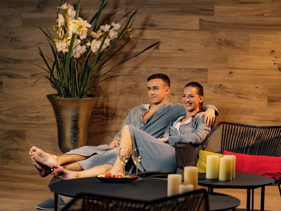 A couple relaxing on a wicker sofa with a potted orchid plant beside them.