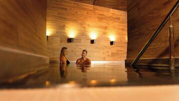 A sauna with wooden walls and a polished floor, featuring two wall-mounted light fixtures.