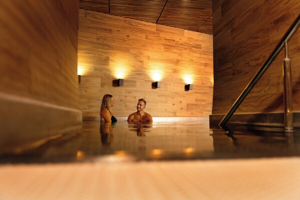 A sauna with wooden walls and a polished floor, featuring two wall-mounted light fixtures. - Lydia Hotel (Tartu)