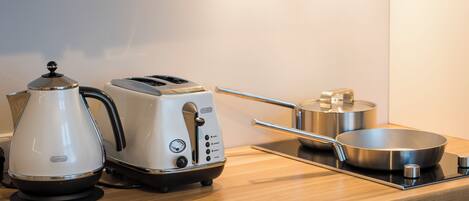Una encimera de cocina con una tetera, un tostador y una sartén sobre una estufa.