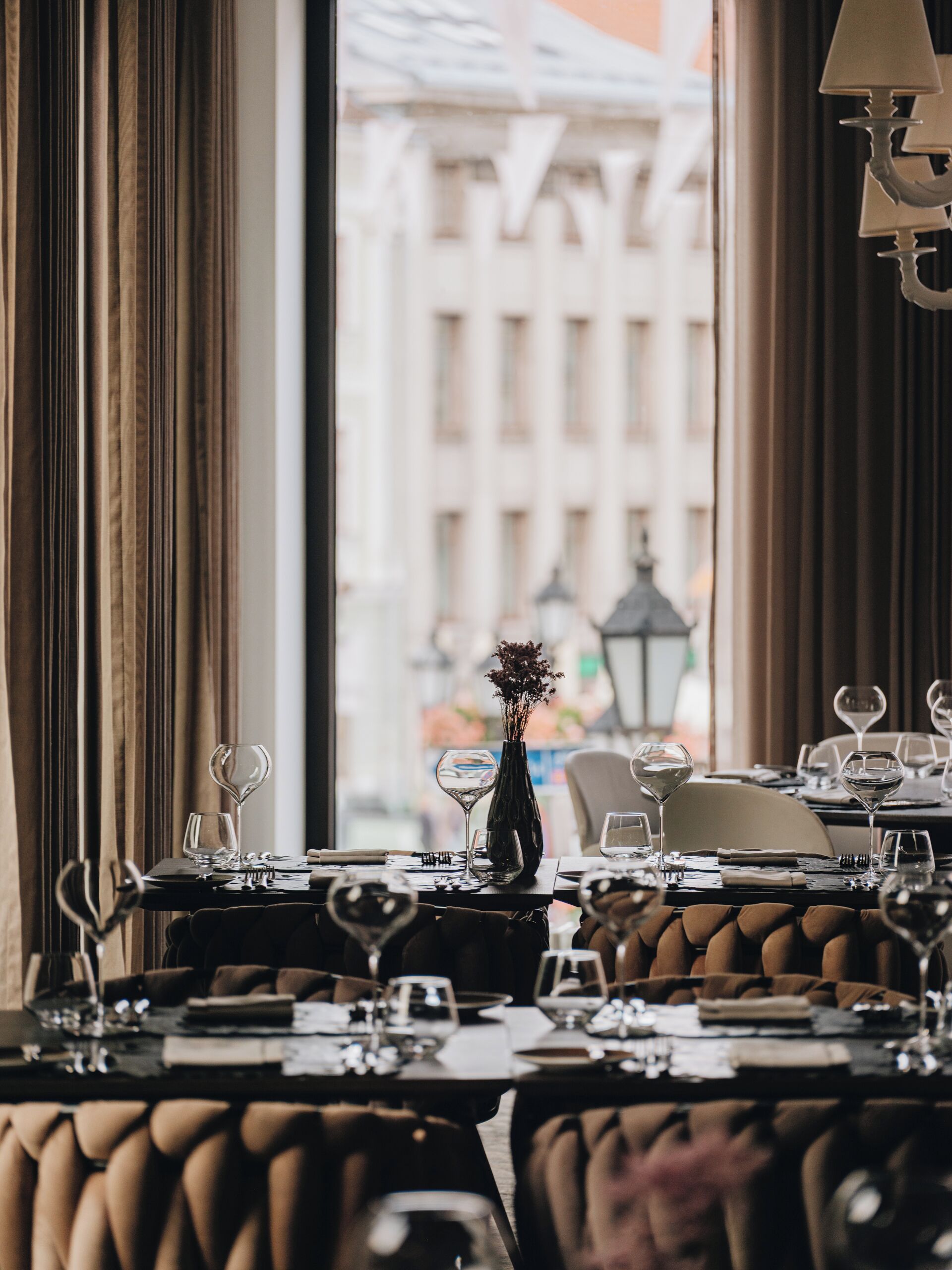 Un restaurante con mesas dispuestas para comer, un jarrón con flores y vistas a edificios a través de la ventana.