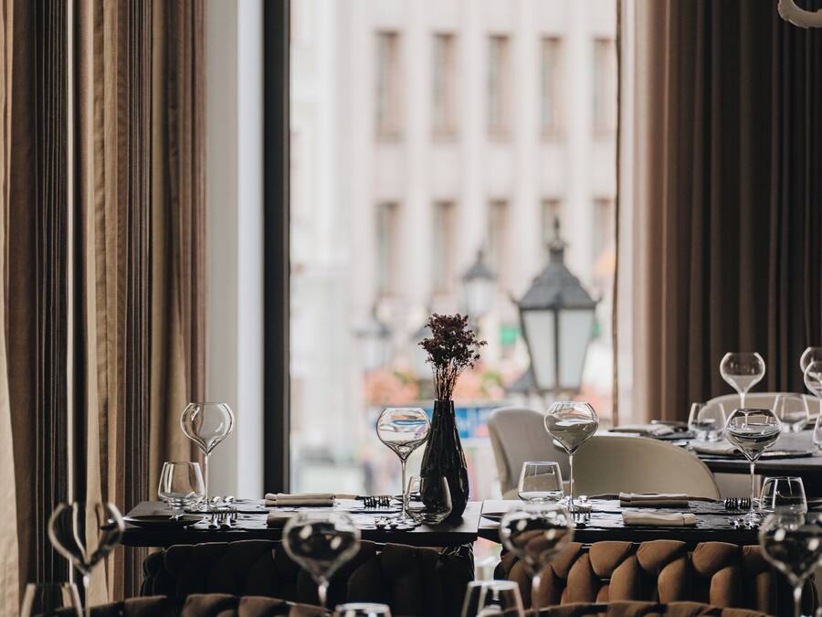 Un restaurante con mesas dispuestas para comer, un jarrón con flores y vistas a edificios a través de la ventana.