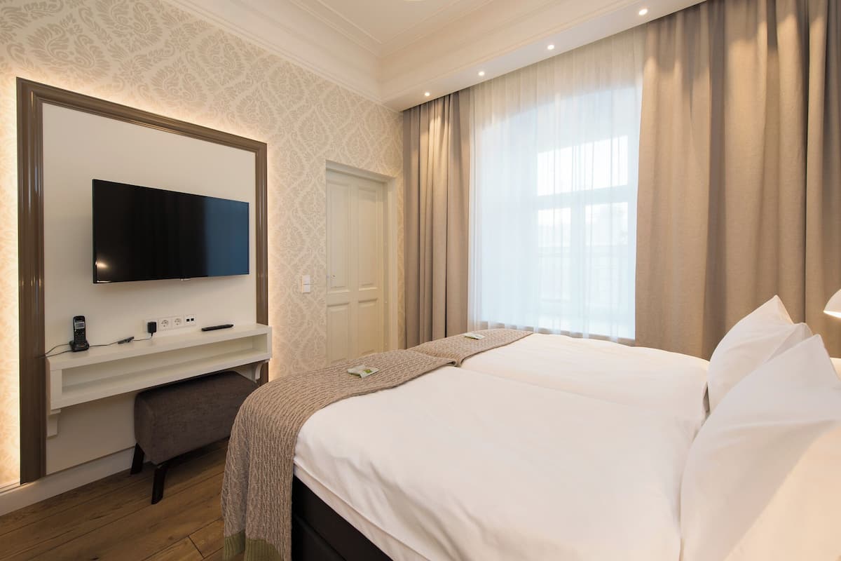 Ein Hotelzimmer mit einem großen Bett, einem an der Wand montierten Fernseher, einem Schreibtisch mit Stuhl und einem Fenster mit Vorhängen.