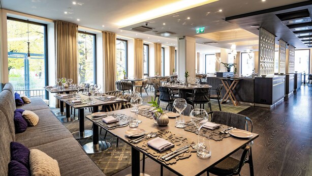 A modern dining area with tables set for a meal, large windows, and a view of the outdoors. - Lydia Hotel (Tartu)