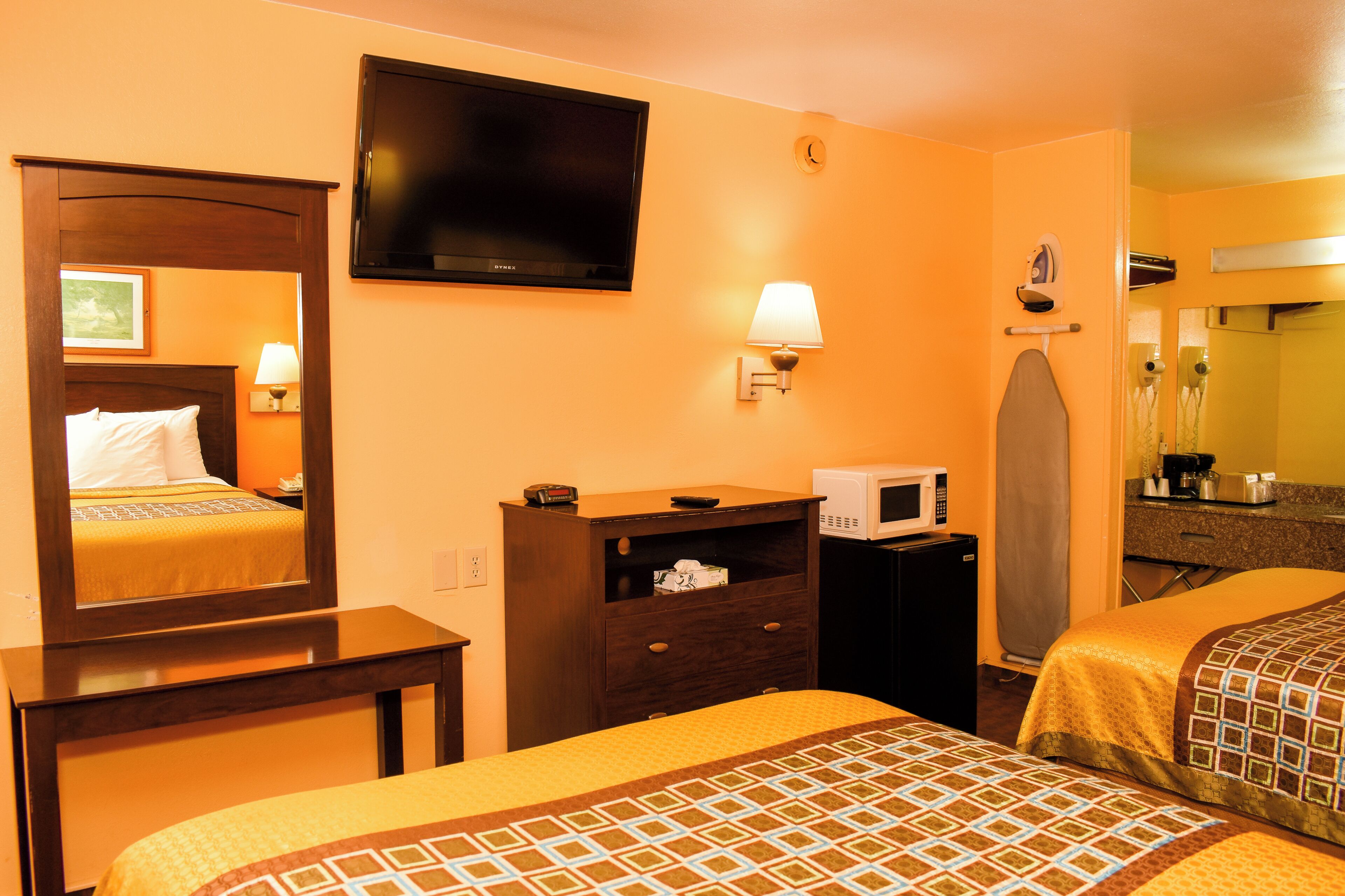 Habitación de hotel con dos camas, televisor, microondas, cómoda y espejo.